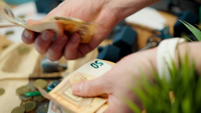 Tangan menghitung uang kertas euro dengan koin berserakan di sekitar.